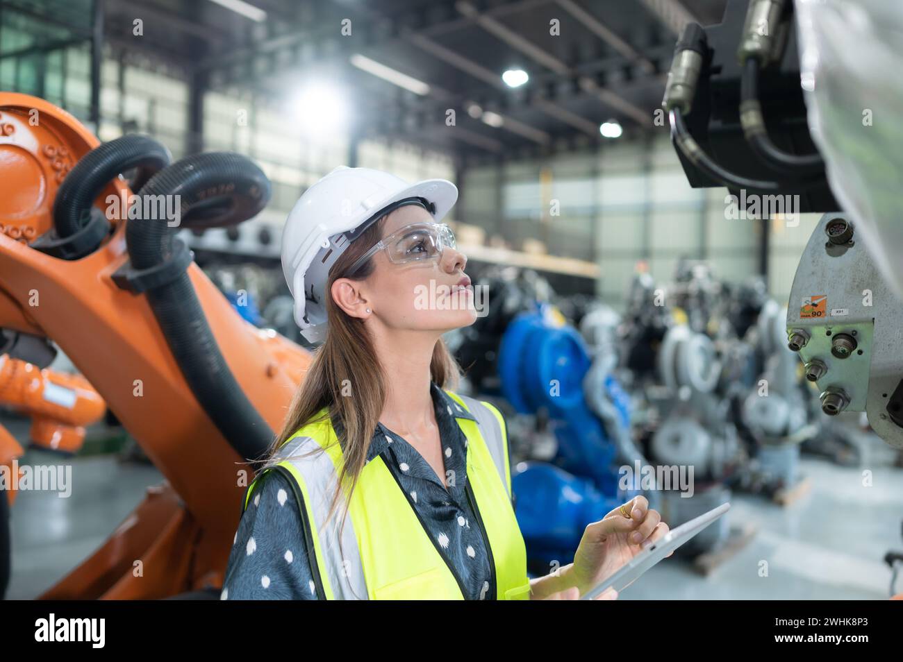 A female engineer installs a program on a robotics arm in a robot warehouse. And test the operation before sending the machine t Stock Photo