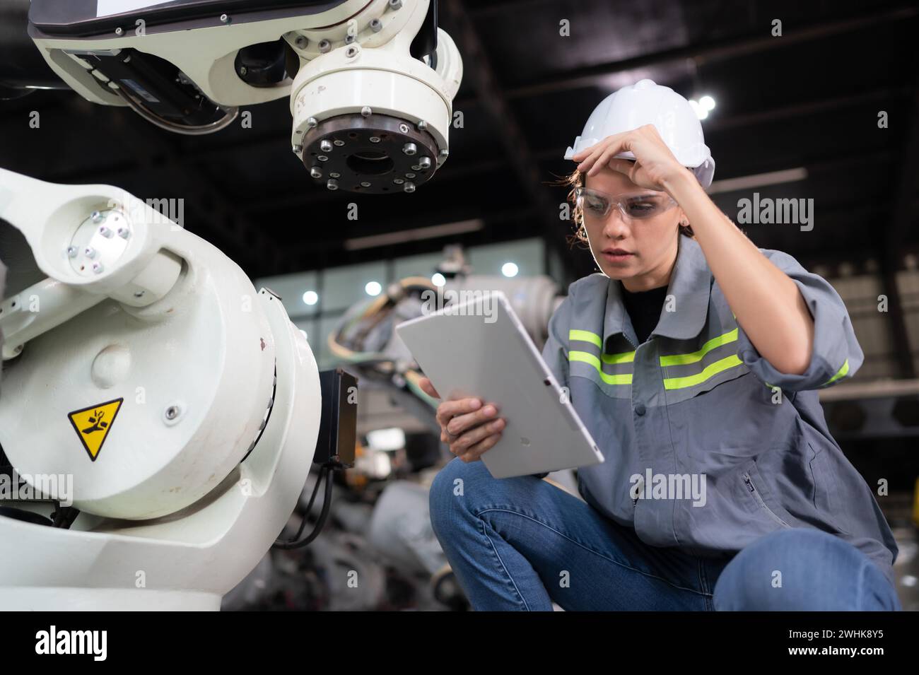 A female engineer installs a program on a robotics arm in a robot warehouse. And test the operation before sending the machine t Stock Photo