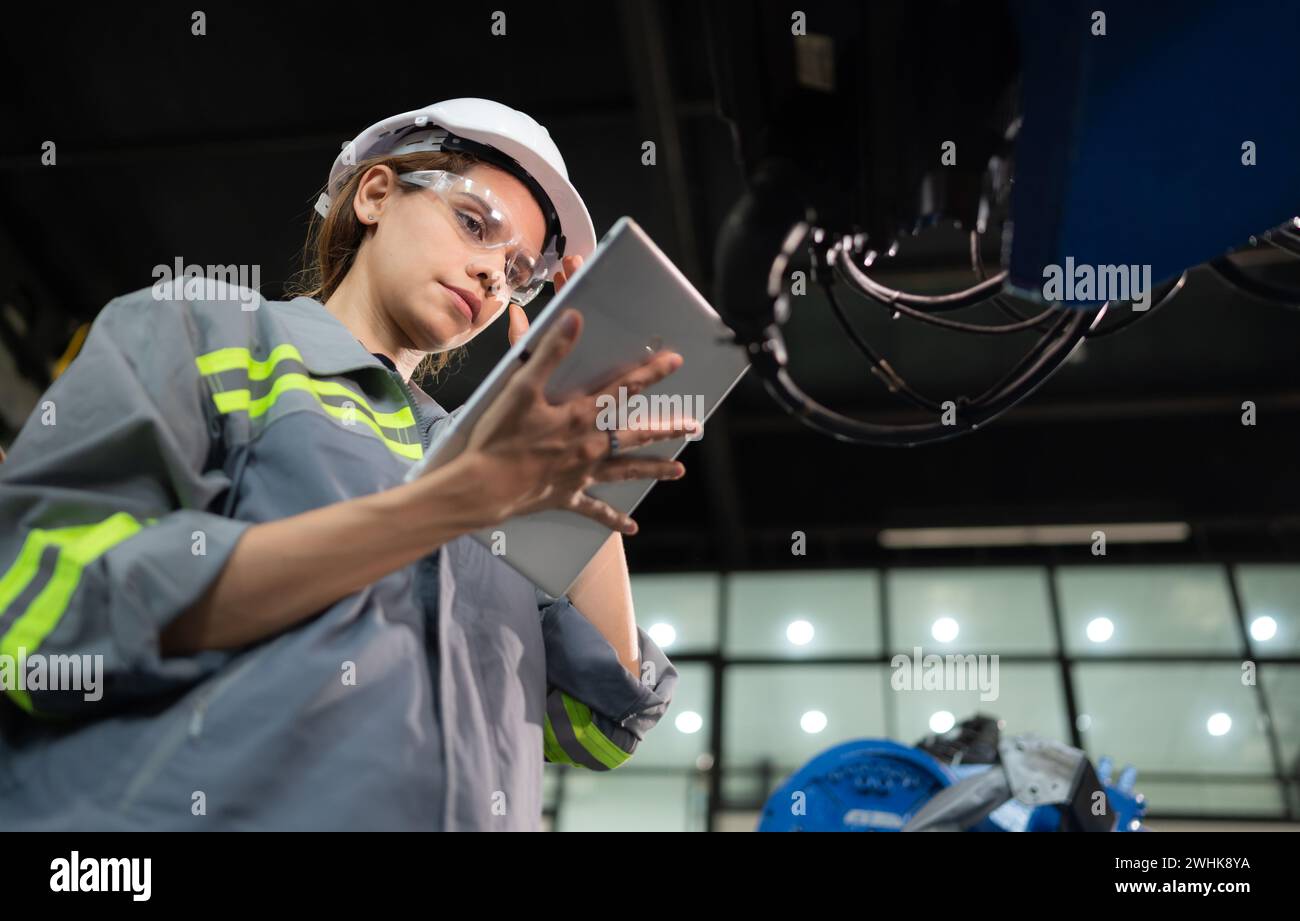 A female engineer installs a program on a robotics arm in a robot warehouse. And test the operation before sending the machine t Stock Photo