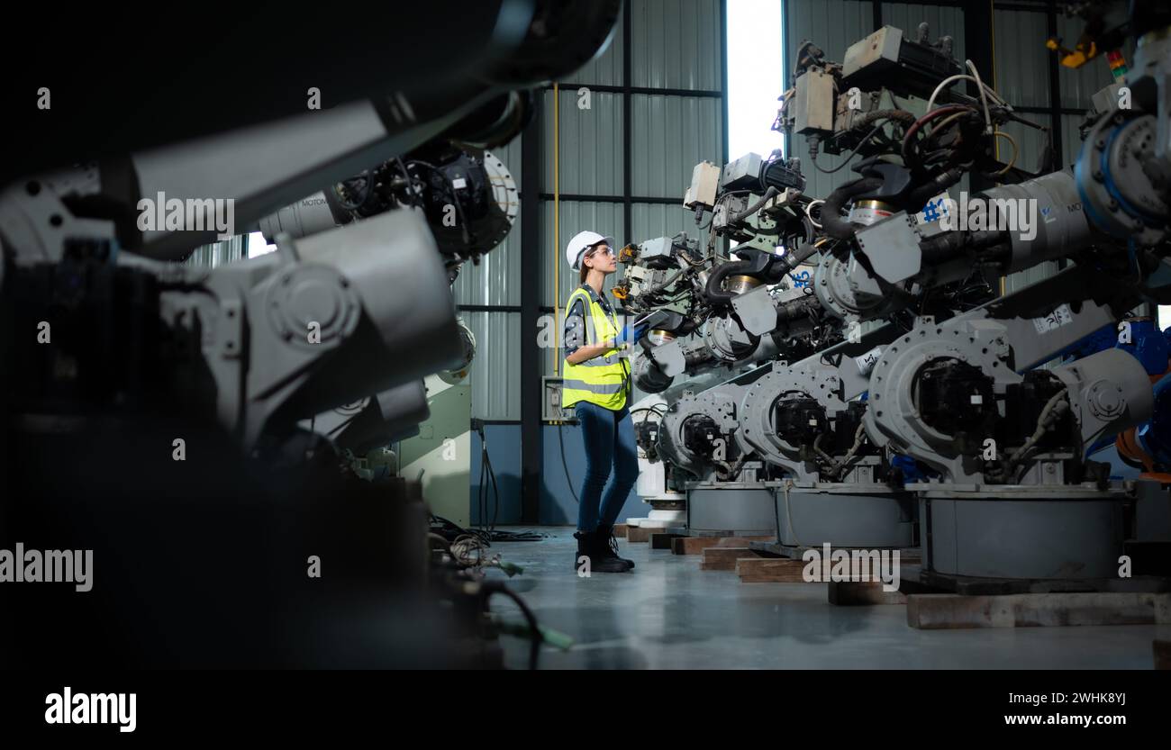 A female engineer installs a program on a robotics arm in a robot warehouse. And test the operation before sending the machine t Stock Photo