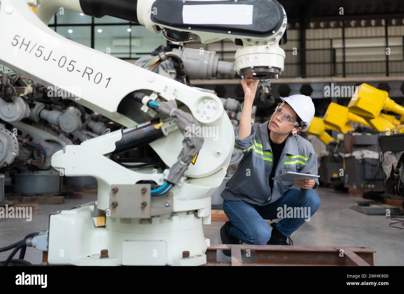 A female engineer installs a program on a robotics arm in a robot warehouse. And test the operation before sending the machine t Stock Photo