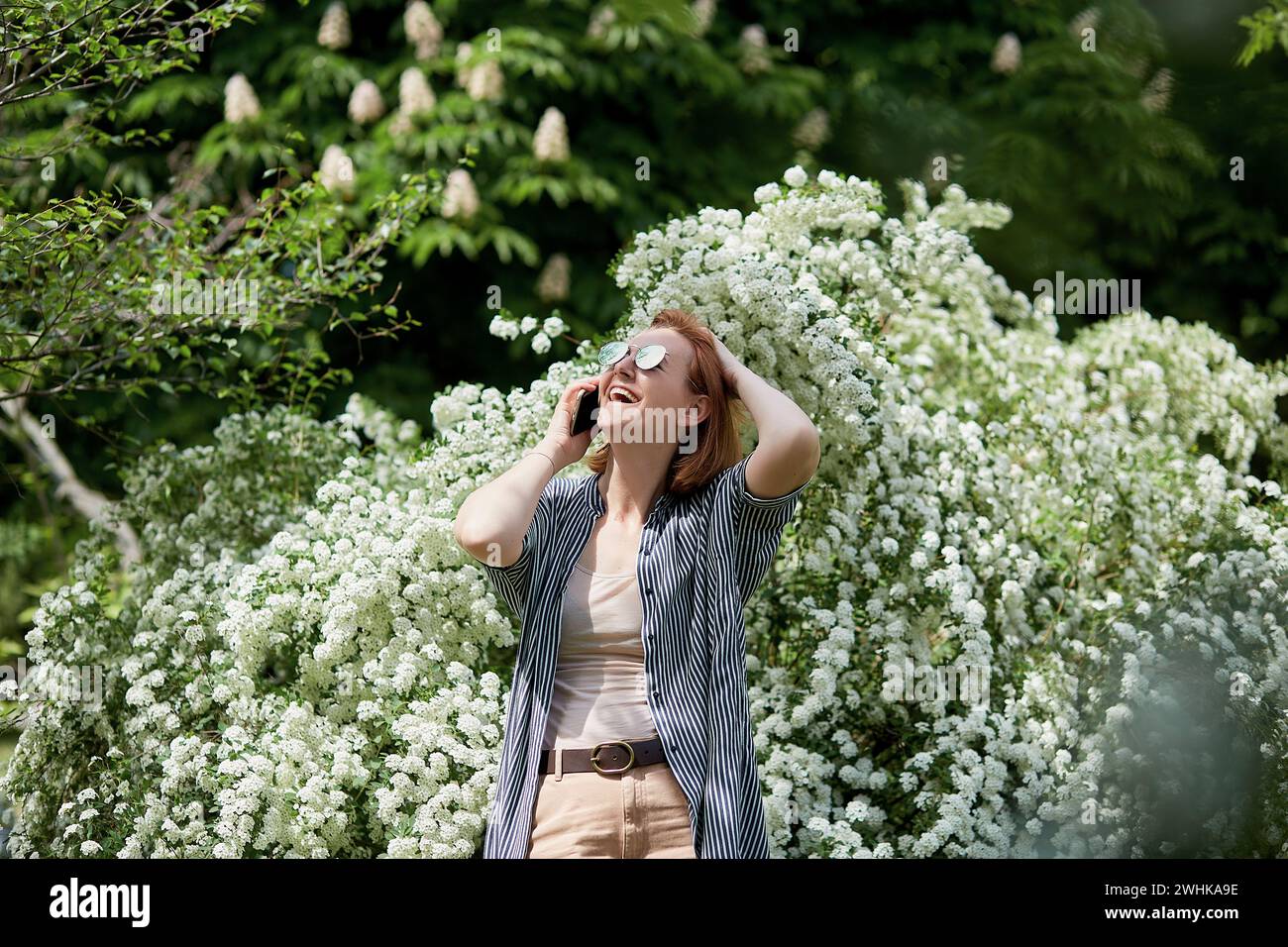 Freelance lifestyle - red-haired woman takes a call surrounded by spring flowers. Stock Photo