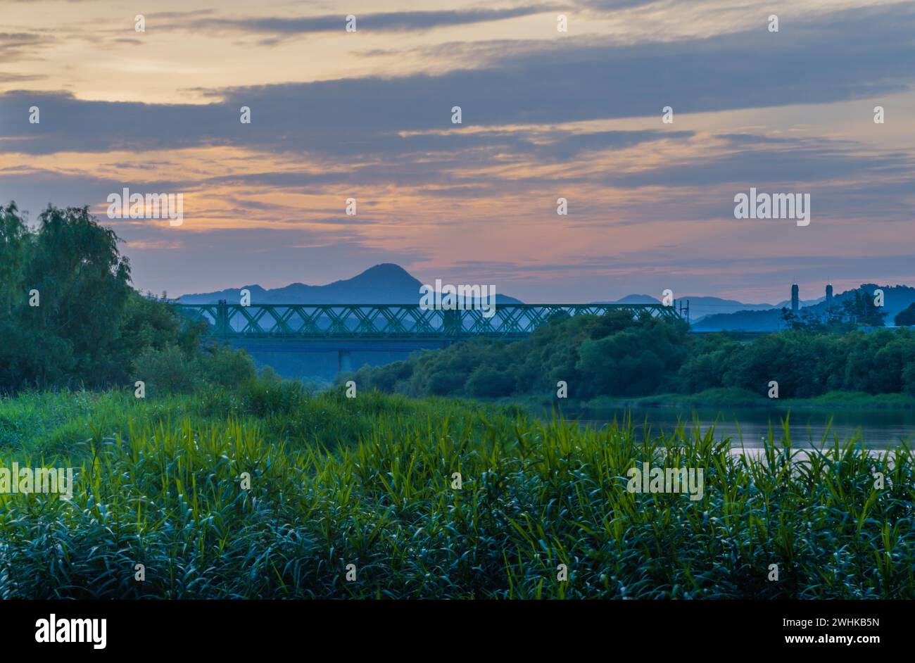 Cloudy morning sky over river in rural setting with railroad bridge and mountain in background in South Korea Stock Photo