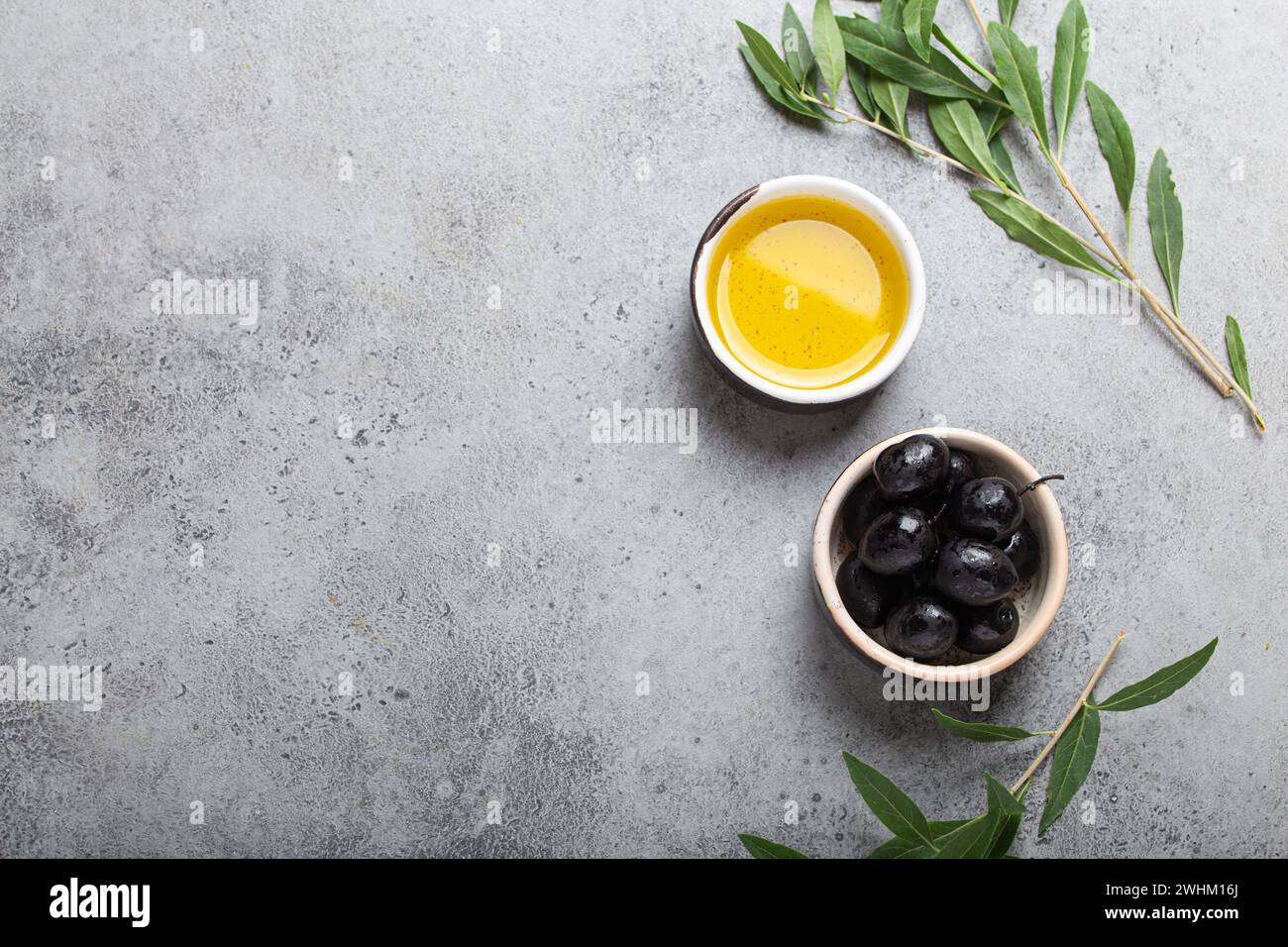 Black olives and extra virgin olive oil in little bowl with olive tree branches top view on grey concrete stone background, spac Stock Photo