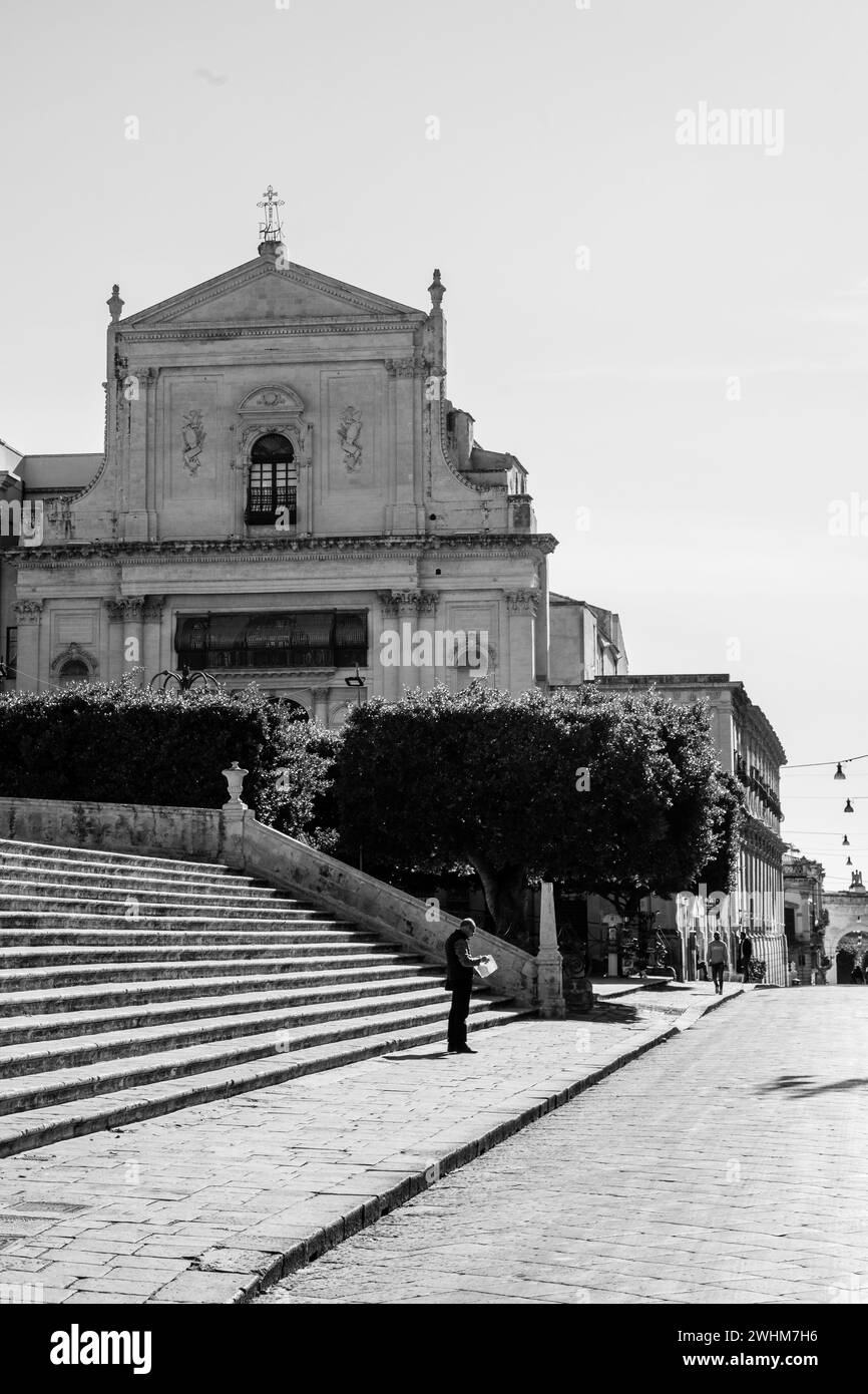 black and white image of the silhouette of a single man standing in Piazza del Dumom, with the Basilica Santissimo Salvatore e Torre in the background Stock Photo