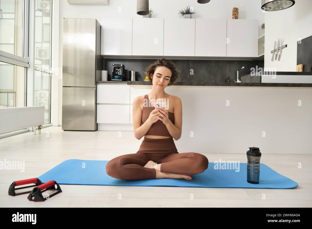 Image of young sport woman sitting at home on yoga mat, doing workout,  stretching fitness exercises on floor in living room, smiling and looking  happy at camera 35338806 Stock Photo at Vecteezy