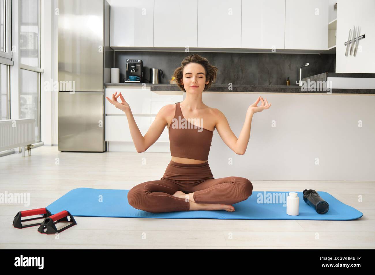 Image of young sport woman sitting at home on yoga mat, doing