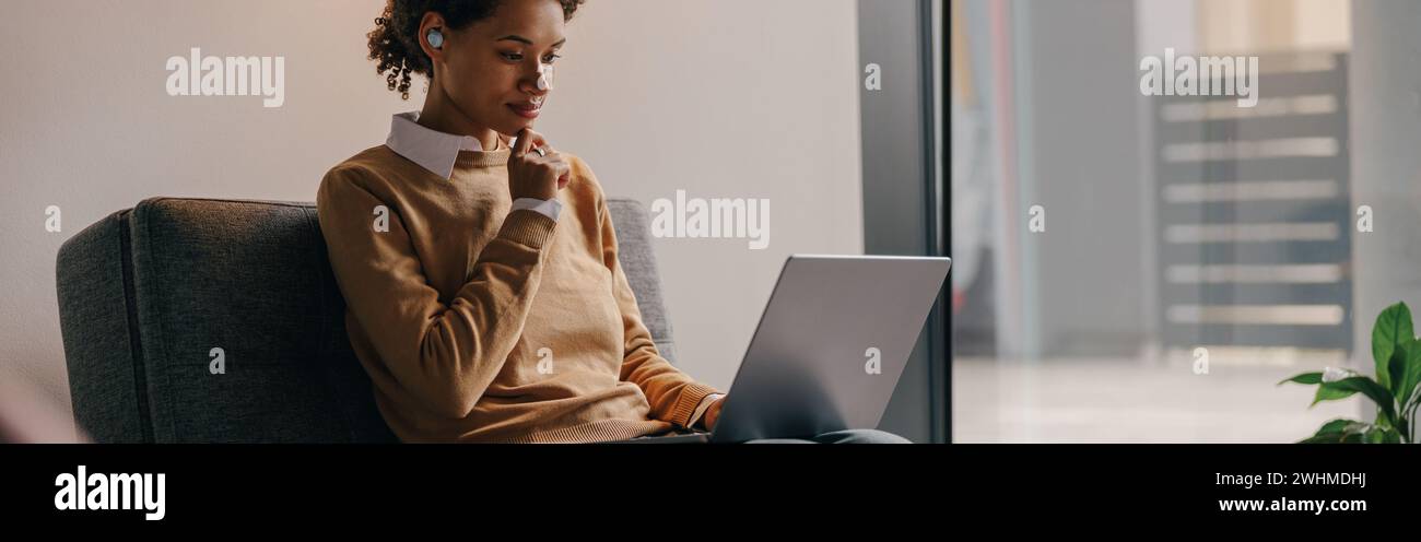Focused female manager using laptop while sitting on cozy office background Stock Photo