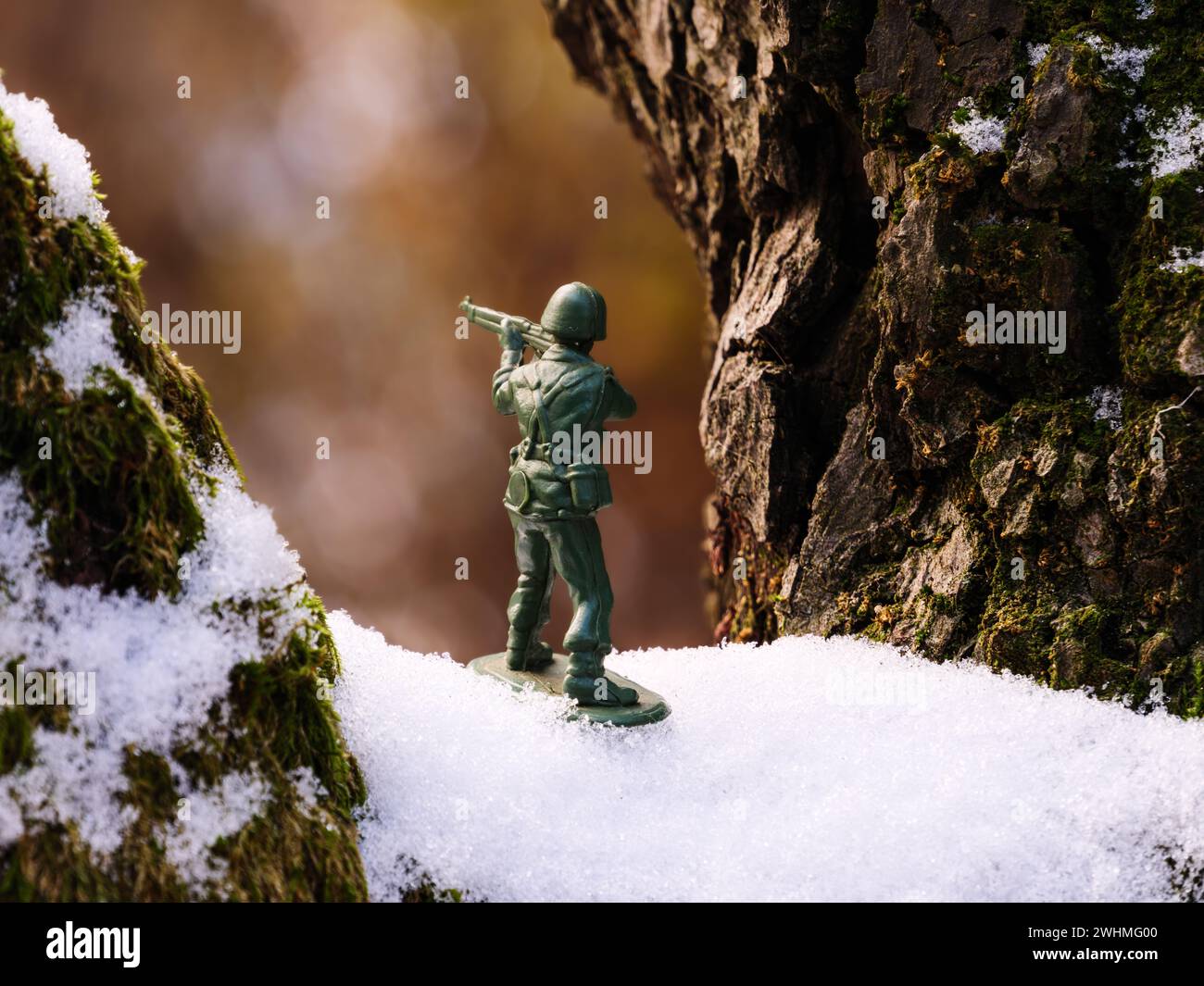 A toy soldier stands on a brown, green mossy, snowy tree branch in the frozen, cold, frosty winter weather. Stock Photo