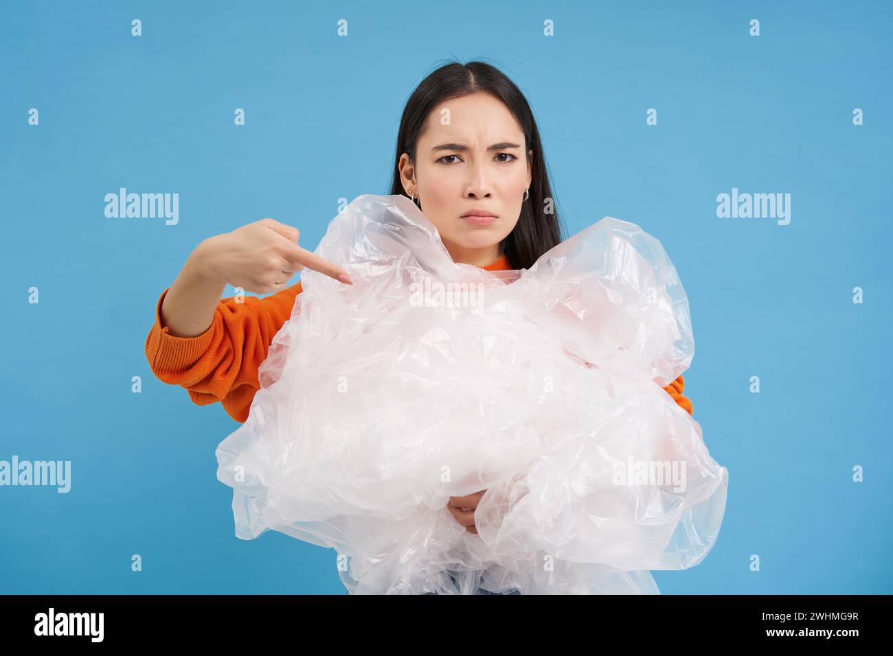 Angry eco-activist points at big pile of plastic bags, fighting to save environment, encourage to recycle and go green, blue bac Stock Photo