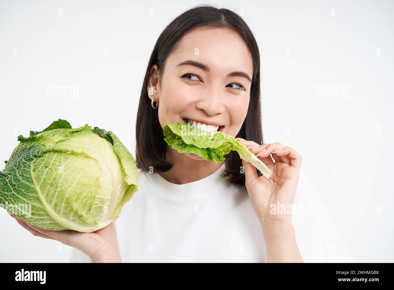Close up of cute korean woman, eating cabbage, on diet, holding lettuce, isolated on white background Stock Photo