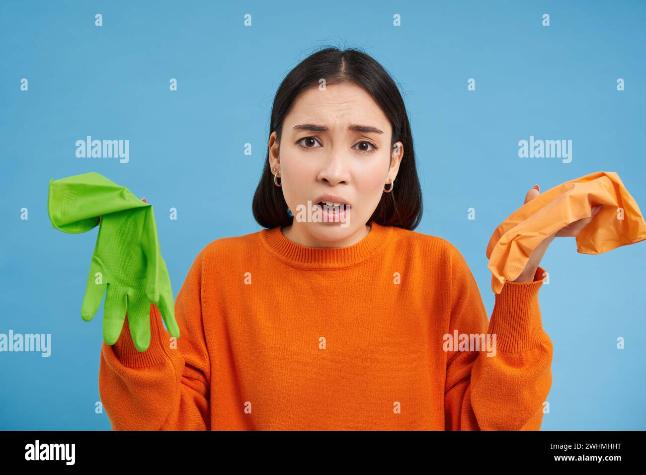Confused asian woman, showing two latex gloves, complains at cleaning