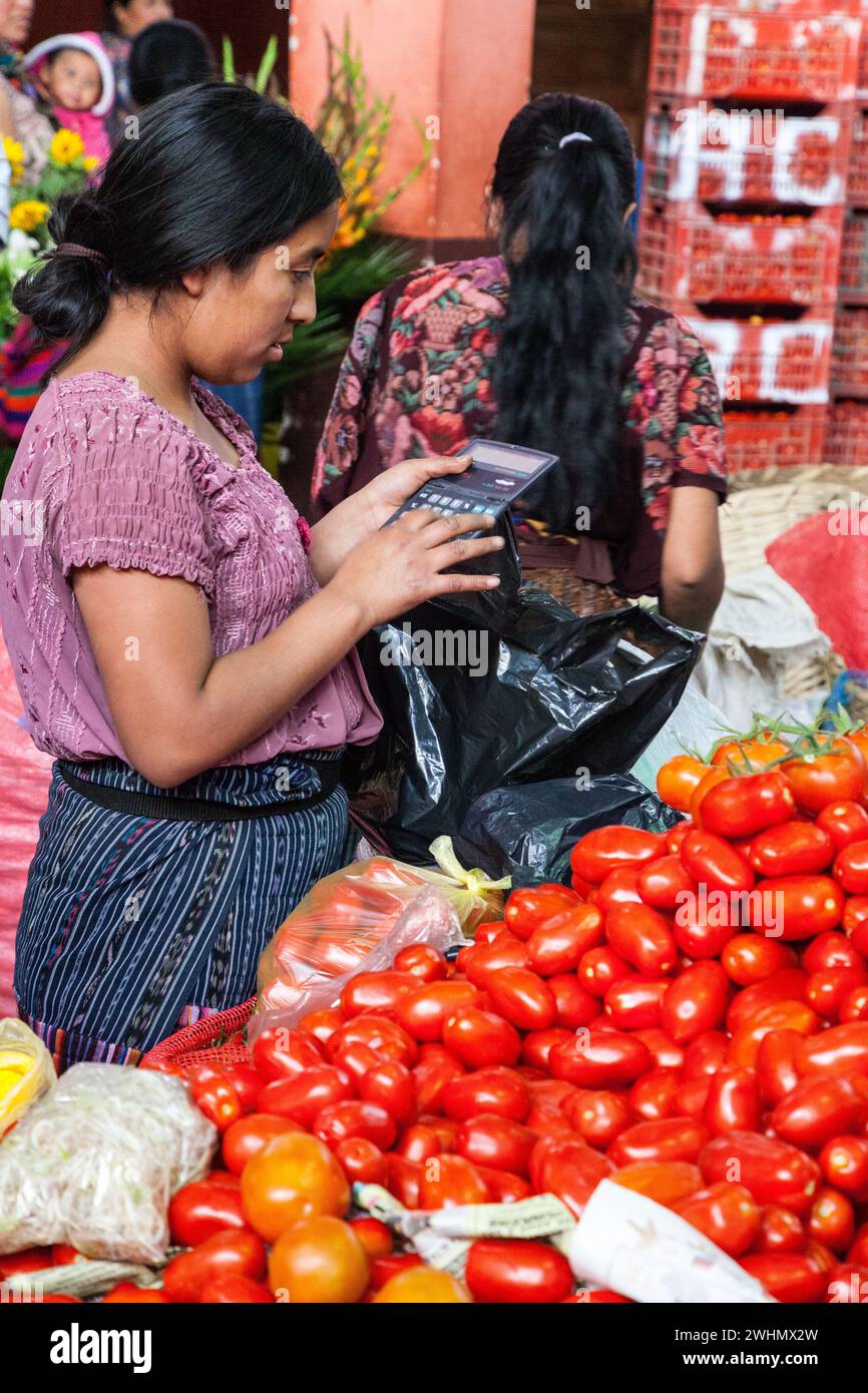 Chichicastenango, Guatemala.  Tomato Vendor Calculating Price of a Sale in the Indoor Market.  Quiche (K'iche') Ethnic Group. Stock Photo