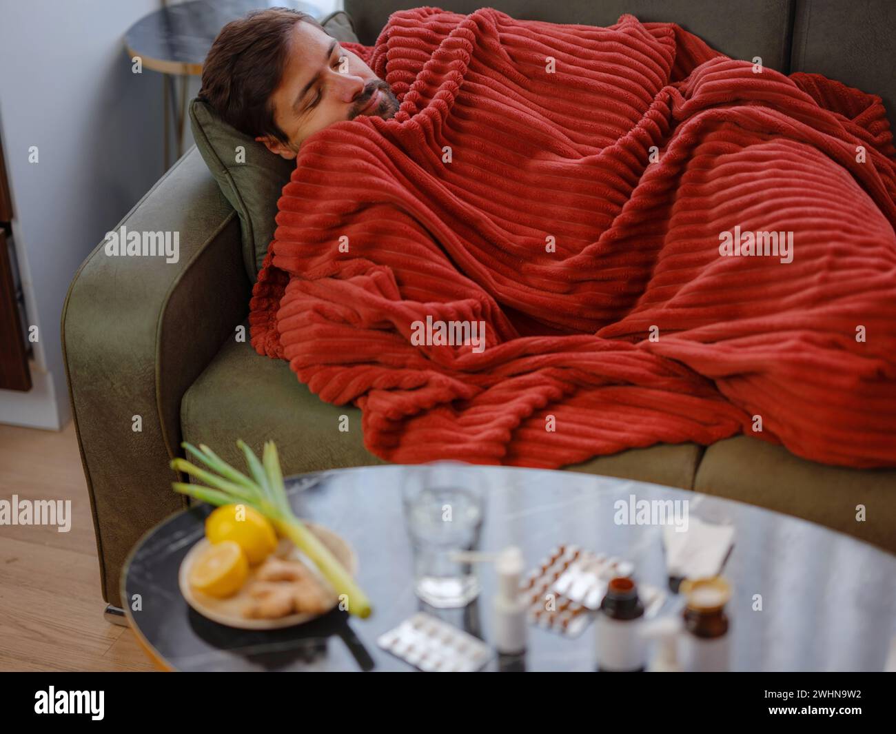 autumn and winter season of sneezes. Young Caucasian Sick man with fever lying on couch . Getting enough restorative sleep helps your body recover and strengthens your immune response. Stock Photo