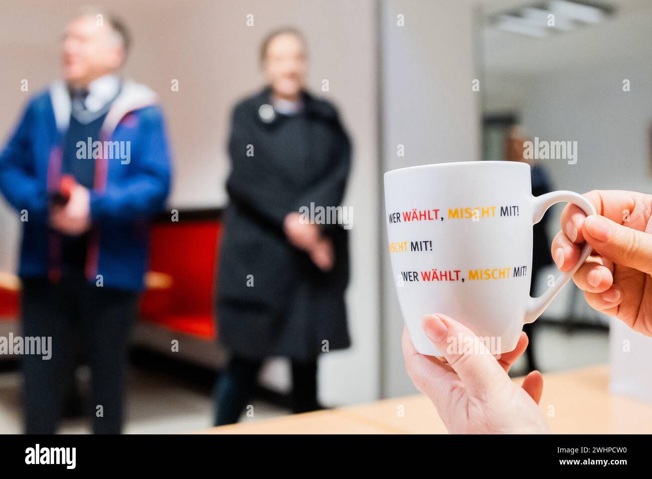 Berlin, Germany. 11th Feb, 2024. A poll worker holds a cup with the inscription 'wer wählt, mischt mit!' (who votes, gets involved!), which she received from the state election officer for Berlin and the federal election officer, at the polling station in the Carl-von-Ossietzky-Gymnasium in Berlin-Pankow. Due to numerous glitches, the 2021 Bundestag election in Berlin will have to be partially repeated. This was decided by the Federal Constitutional Court on December 19, 2023. Credit: Christoph Soeder/dpa/Alamy Live News Stock Photo