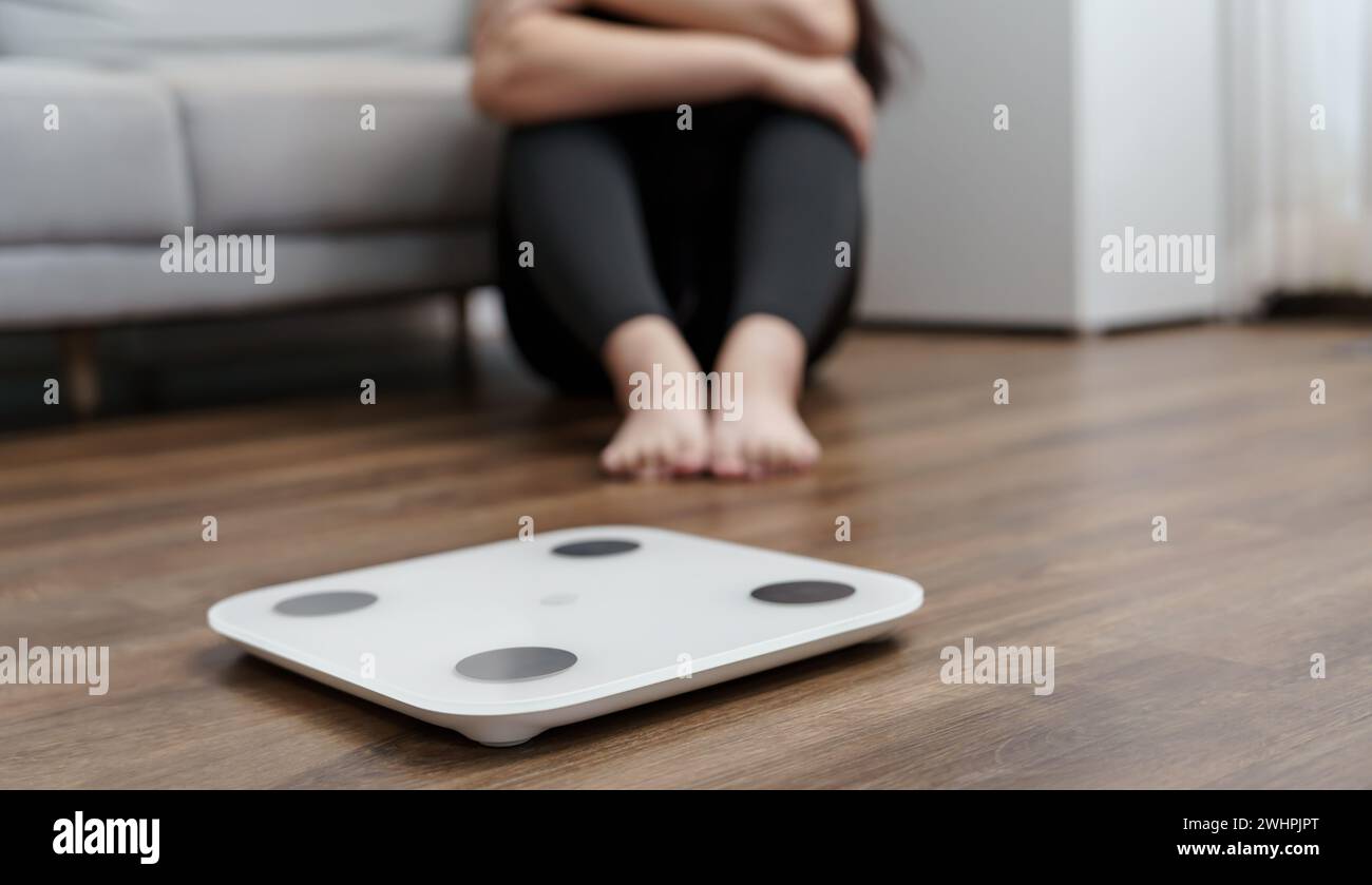 Sad woman with fat upset bored of dieting Weight loss failÂ  Fat diet and scale sad asian woman on weight scale at home weight c Stock Photo