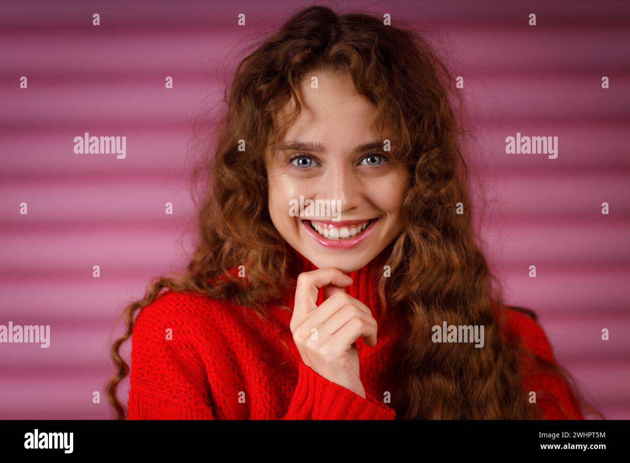 Happy smiling young adult woman wearing winter red sweater indoors looking at camera with joyful smile. Stock Photo
