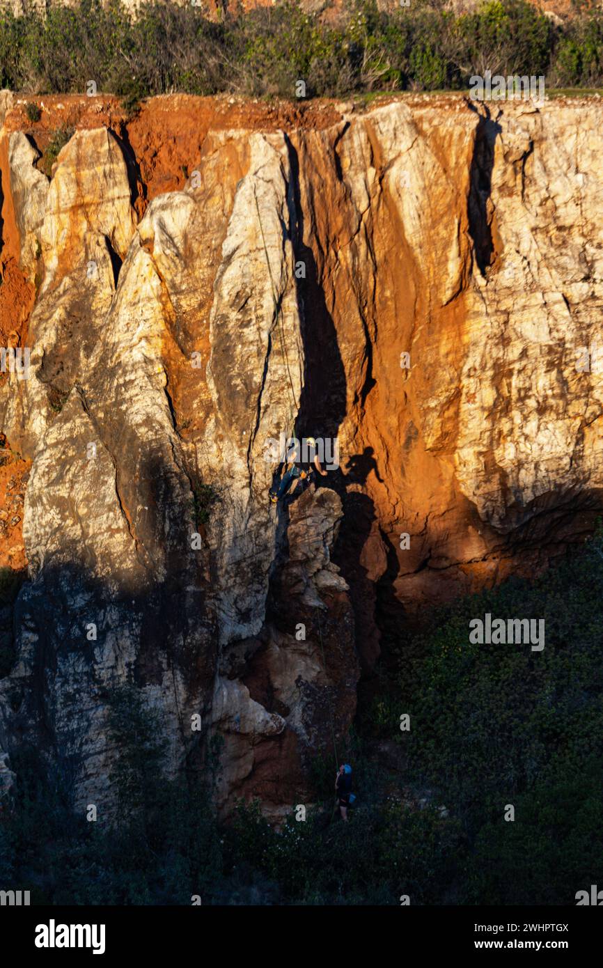 Man climbing rock wall attached by ropes to his partner. Silhouette of a climber reflected in the rock. Stock Photo