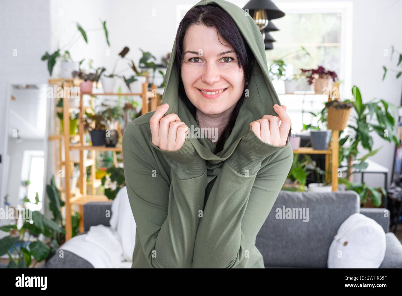 Large portrait Joyful emotions of a woman in the hood in her home in a bright modern interior with home plants. Eco-friendly por Stock Photo