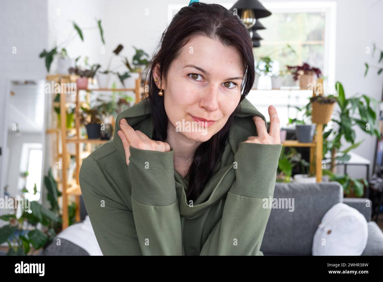 Large portrait Joyful emotions of a woman in the hood in her home in a bright modern interior with home plants. Eco-friendly por Stock Photo
