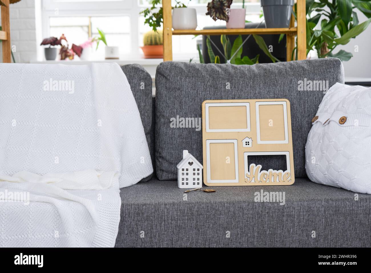 Key to home with keychain and mock up frame miniature of house on gray sofa in white interior with potted plants. Design, projec Stock Photo