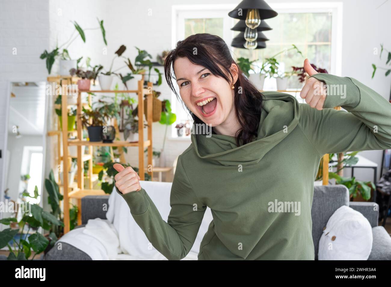 Joyful emotions of a woman in her home in a bright modern interior with home plants. Eco-friendly portrait with real joy Stock Photo