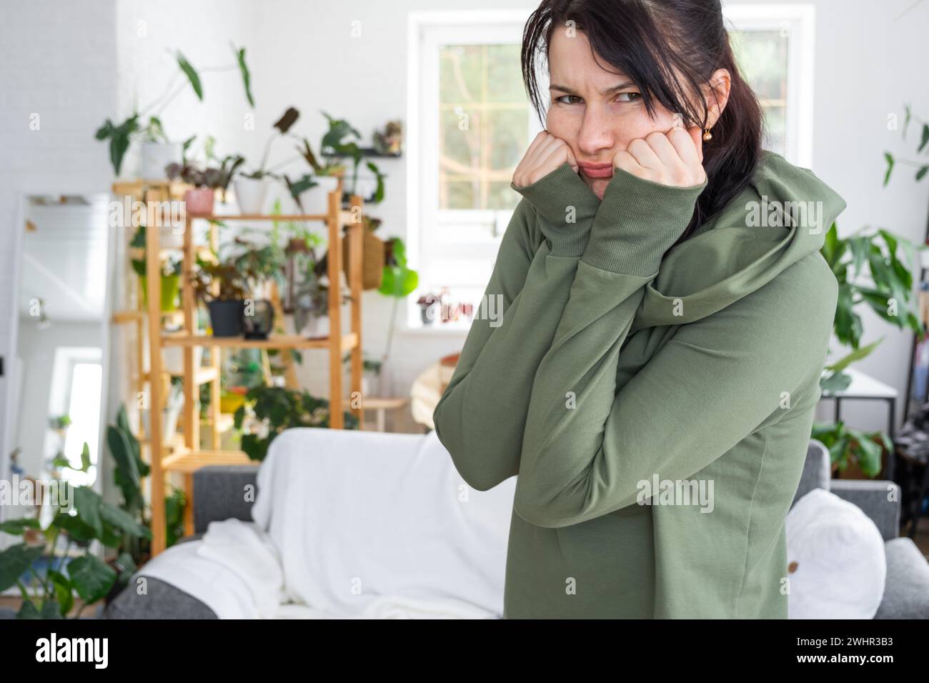 Distressed and Thoughtful emotions of a woman in her home in a bright modern interior with home plants. Portrait of a upset and Stock Photo