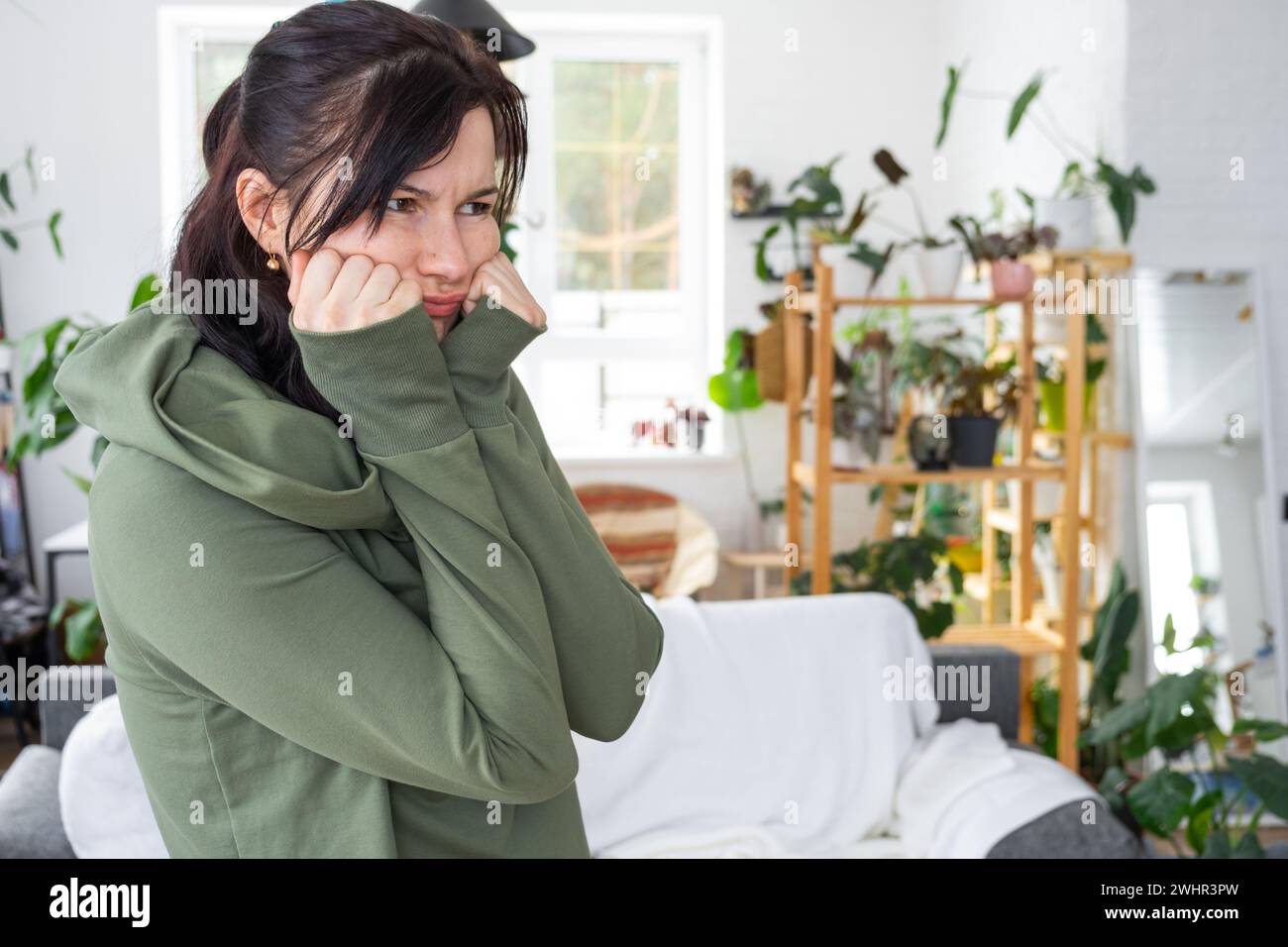Distressed and Thoughtful emotions of a woman in her home in a bright modern interior with home plants. Portrait of a upset and Stock Photo