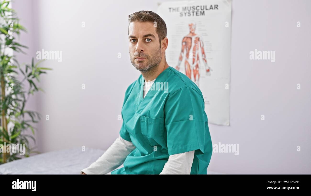 Handsome bearded hispanic man in scrubs posing inside a clinic with a muscular system chart in the background. Stock Photo
