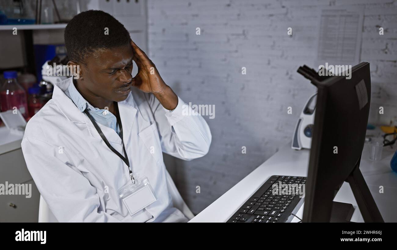 Stressed african man in lab coat analyzing data on computer in modern ...