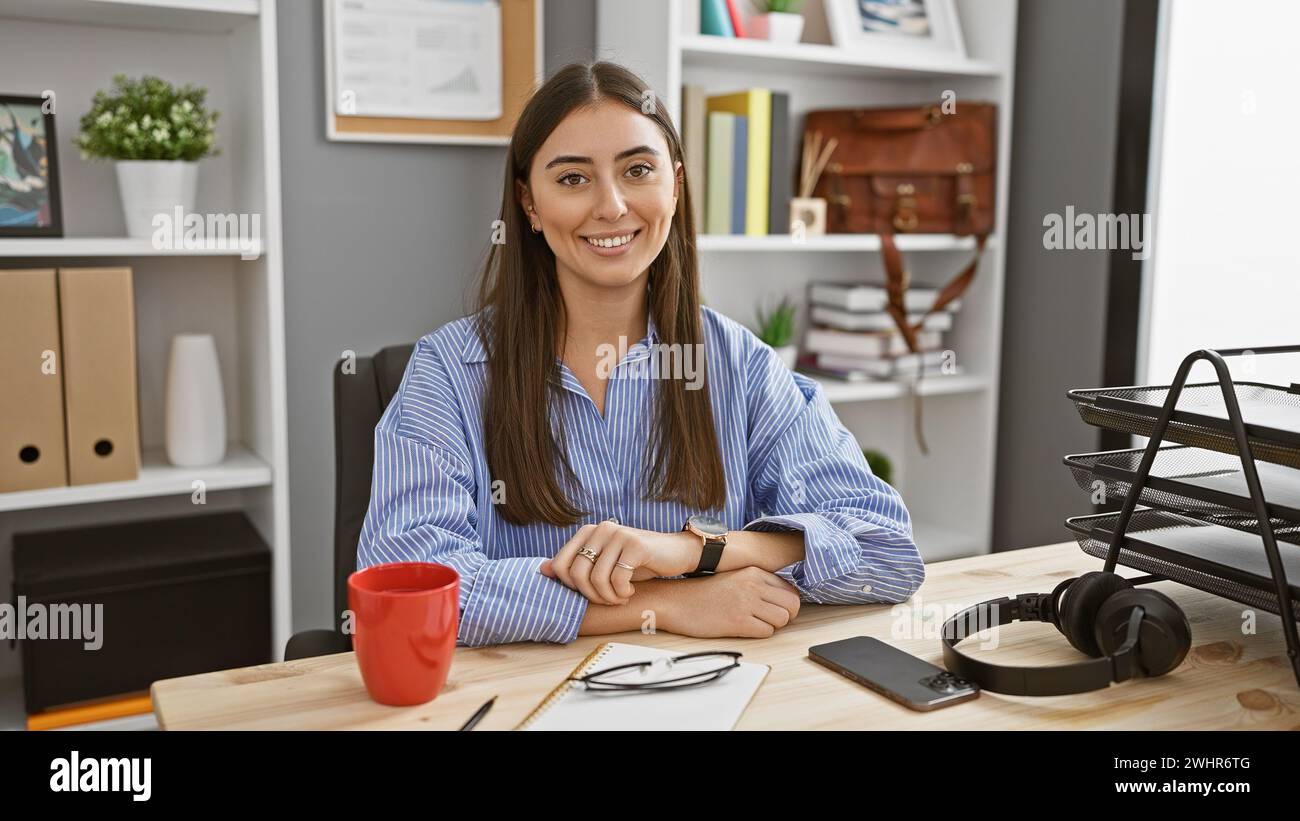 Portrait of a smiling young hispanic woman in a business office, wearing professional attire and accessories. Stock Photo
