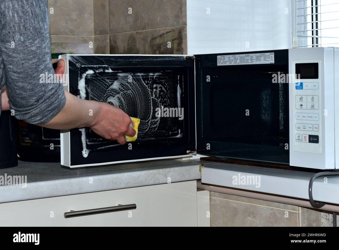 A woman washes the microwave oven with a sponge and detergents. High quality photo Stock Photo