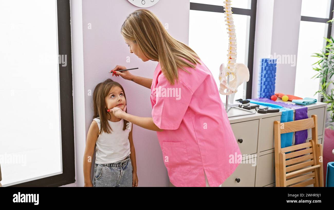 Pediatrician in pink measuring girl's height in clinic interior. Stock Photo