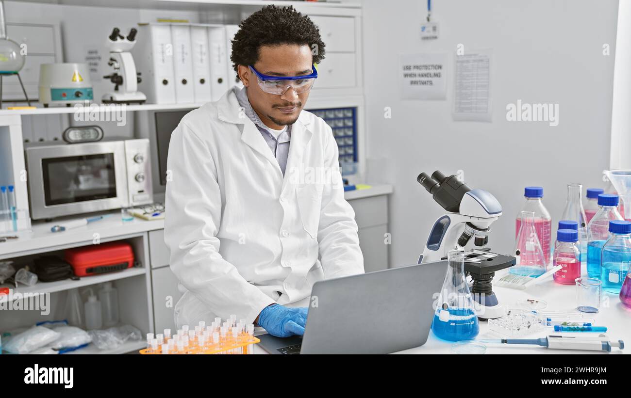A young adult man with curly hair wearing lab coat and safety goggles ...