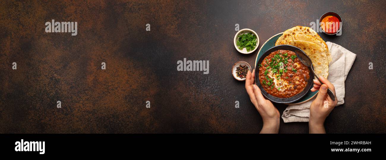 Female hands holding a bowl, eating traditional Indian Punjabi dish Dal makhani with lentils and beans served with naan flat bre Stock Photo