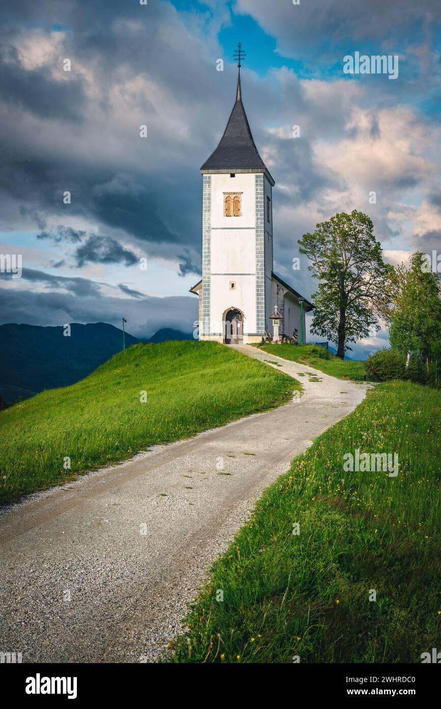 Spring scenery and traditional church on the hill. Fantastic place with rural road and Saint Primoz church in background, Jamnik village, Slovenia, Eu Stock Photo