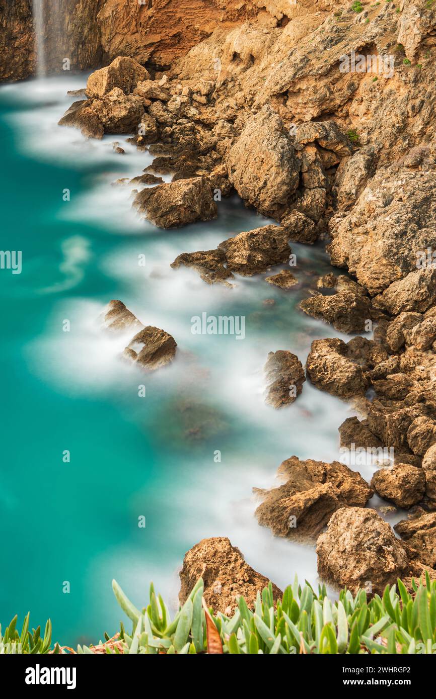 Long exposure photo of waves hitting the rocks of the cliff Stock Photo
