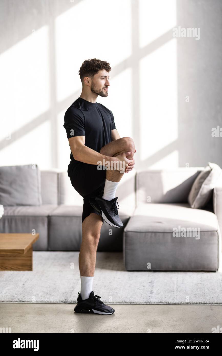 Handsome young man with athletic body doing squats at home Stock Photo