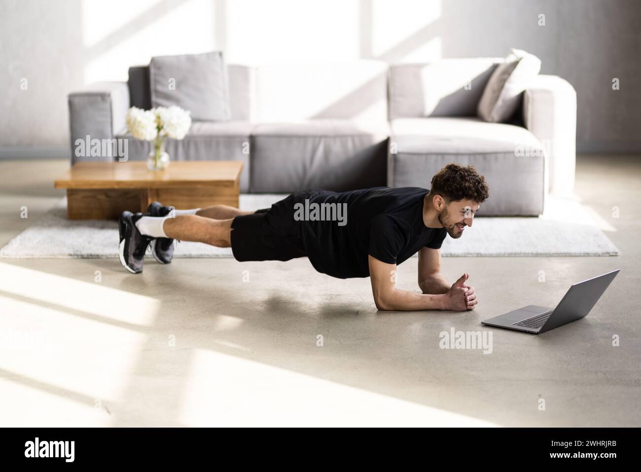 Online workout. Young man doing plank exercise with online tutorial at home, panorama, free space Stock Photo