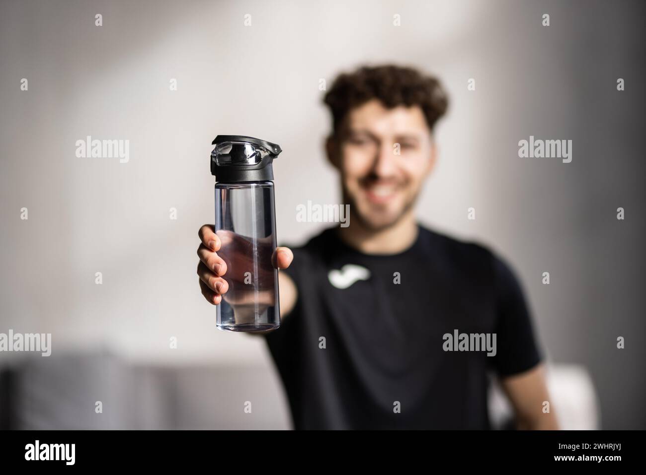 Sporty man with headphones drinking water after his workout at home. Healthy lifestyle, wellness concept Stock Photo