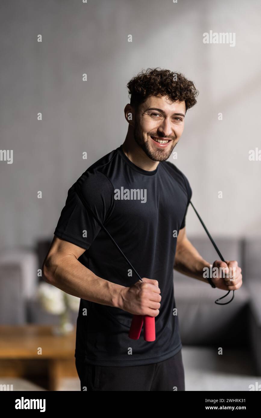 fitness, sport, exercising and healthy lifestyle concept. Young man skipping with jump rope at home Stock Photo