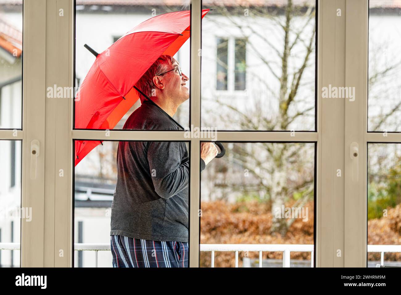 Regenwetter, Mann steht mit Regenschirm auf seinem Balkon, München, Februar 2024 Deutschland, München, Februar 2024, Regenwetter vorhergesagt, älterer Mann steht im Regen auf seinem Balkon, hat den Regenschirm aufgespannt und schaut skeptisch zum Himmel, fragt sich, ob er bei dem Mistwetter nicht gleich zuhause bleibt oder wieder ins Bett legt, schlechtes Wetter, Wochenende, Winter, Bayern *** Rainy weather, man stands with umbrella on his balcony, Munich, February 2024 Germany, Munich, February 2024, rainy weather forecast, elderly man stands in the rain on his balcony, has opened the umbrell Stock Photo