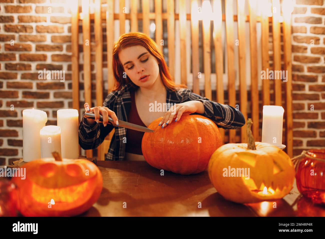 Young woman making Halloween pumpkin Jack-o-lantern. Female hands cutting pumpkins with knife. Stock Photo