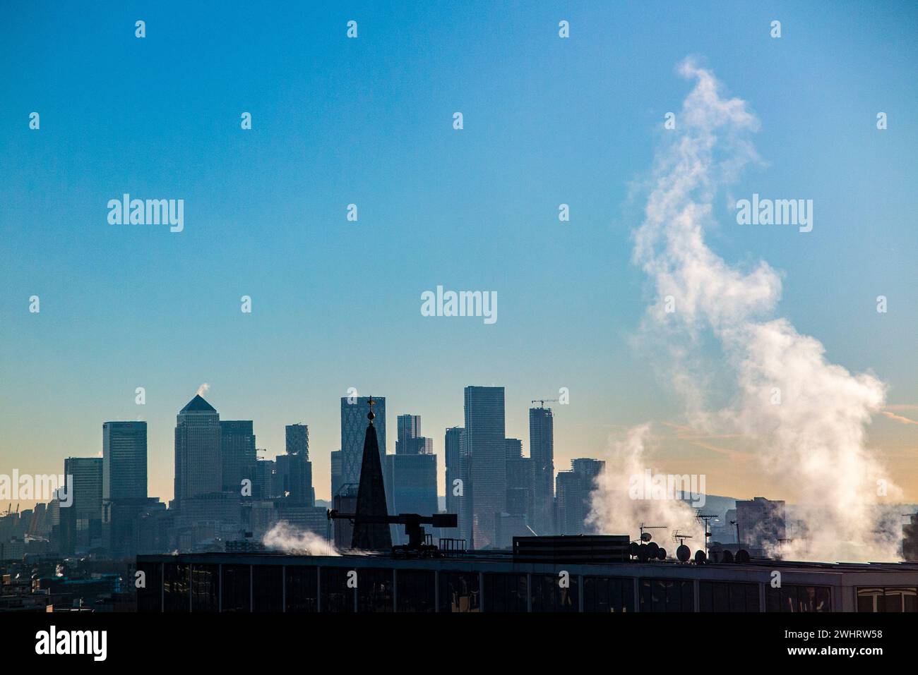 Plumes of steam rising from an office in the City of London with Canary Wharf and the Docklands in the distance Stock Photo