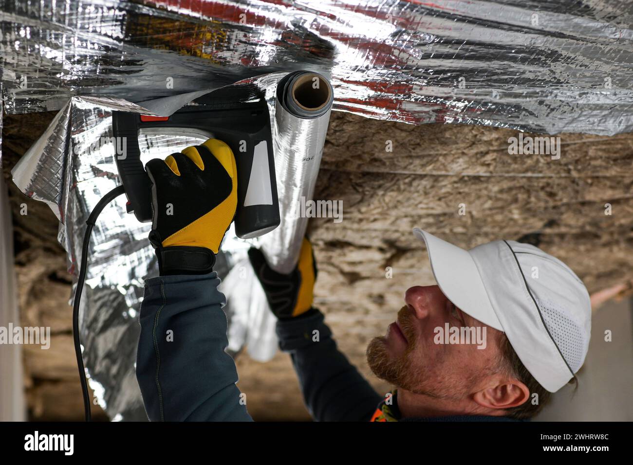 construction worker staples the vapor barrier to the ceiling Stock