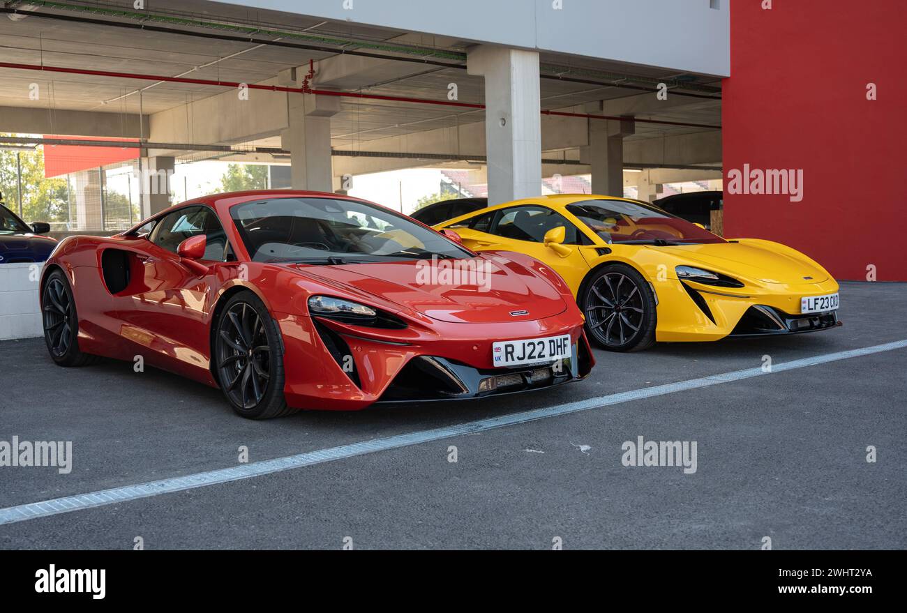 Front view of a pair of modern McLaren Artura supercars, one red and the other yellow Stock Photo