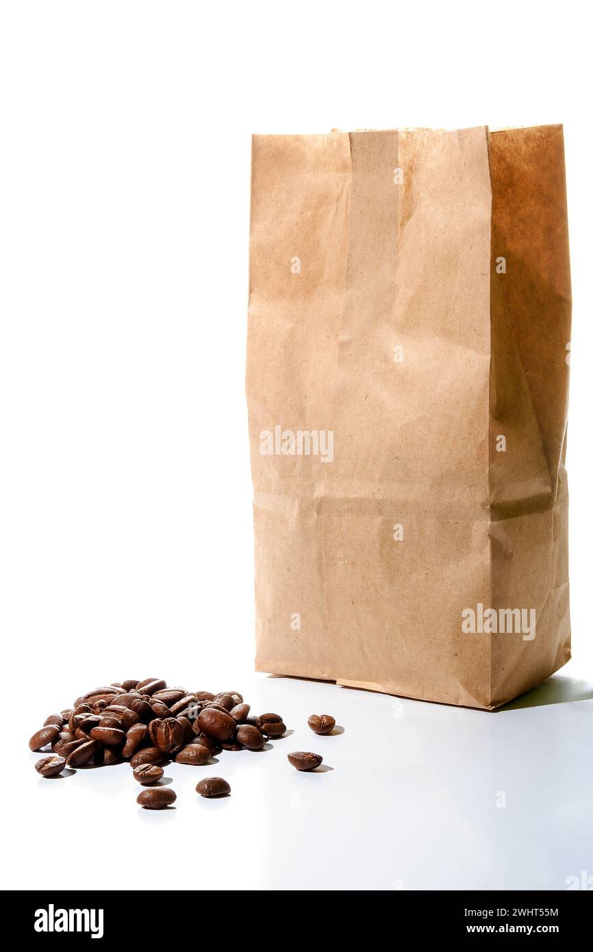 roasted coffee beans spilled in front of a brown disposable package made from craft paper on the white background. recyclable and sustainable mockup c Stock Photo