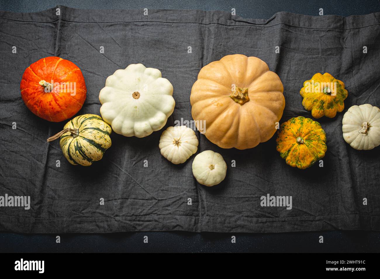 Thanksgiving festive table composition with different pumpkins on gray tablecloth runner, rustic dark table top view. Stock Photo