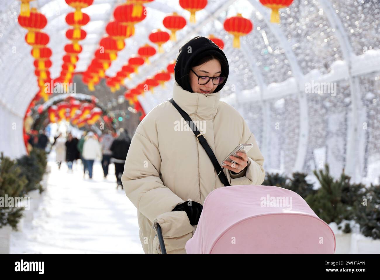 Girl with smartphone walking with baby stroller on background of Chinese New Year decorations in winter city Stock Photo