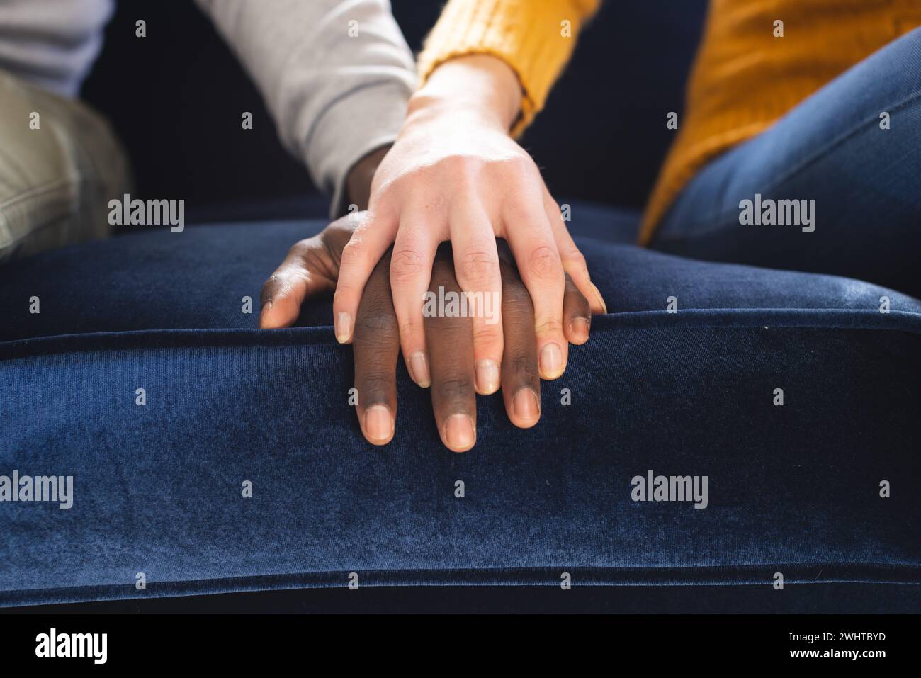 Midsection of diverse couple sitting on sofa holding hands at home Stock Photo